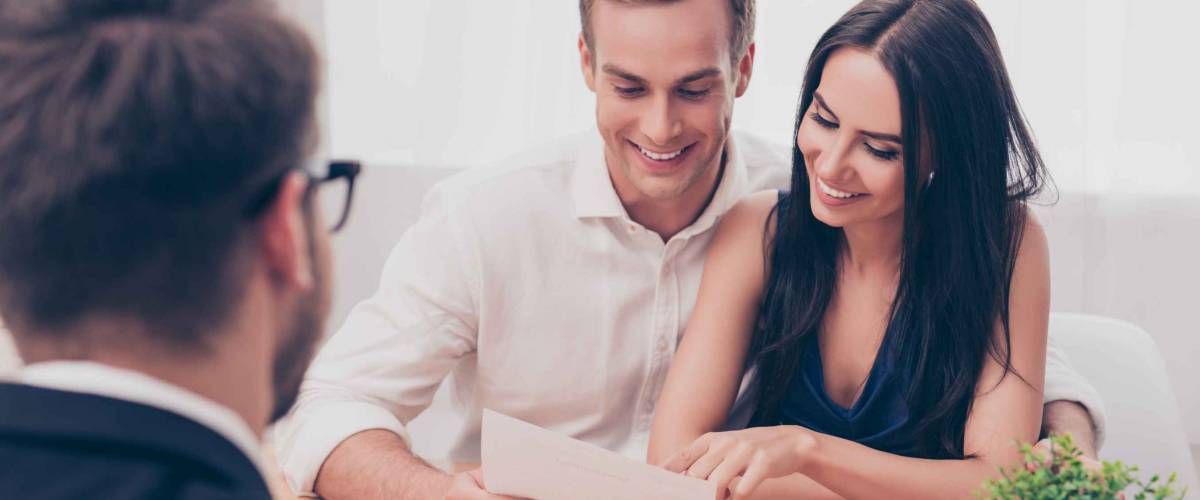man and woman smile looking at a piece of paper, sitting across from a man in a suit