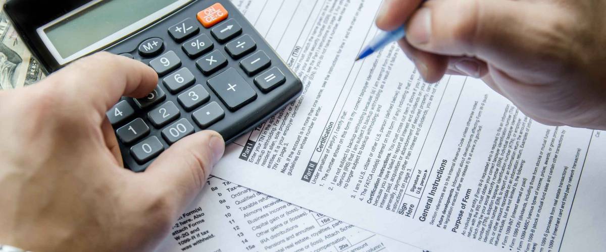 image of man's hands filling out tax forms with the use of a calculator