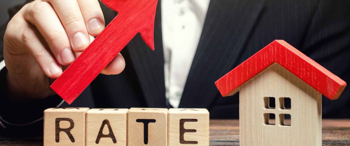 A man holds a red arrow up above the word Rate and a wooden house.