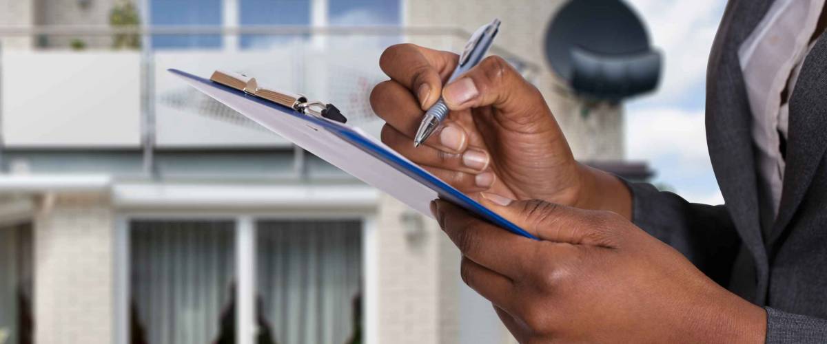 Close-up Of A Person's Hand Filling Document In Front Of House