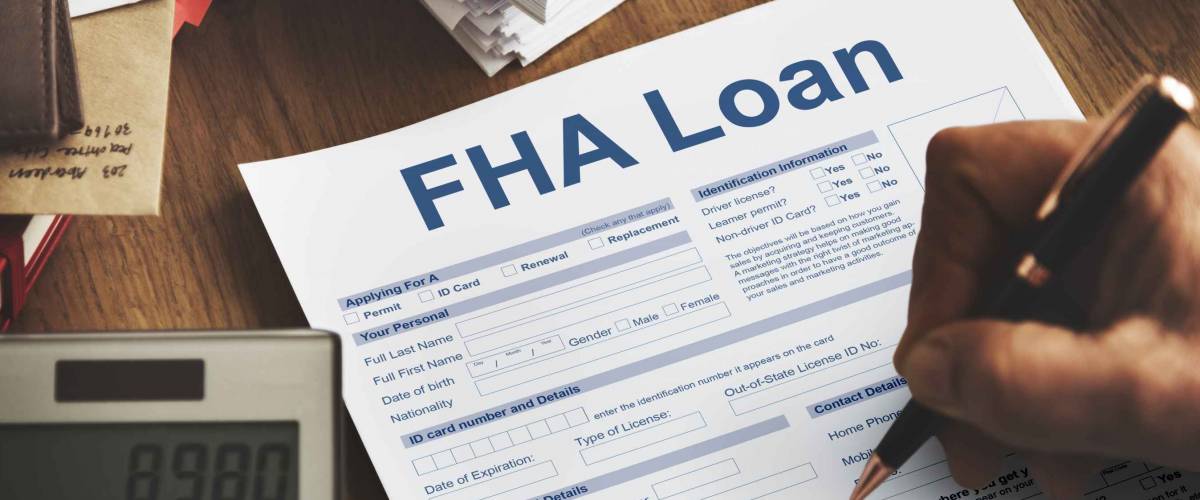 Person's hand holding pen over paper with FHA loan written on it