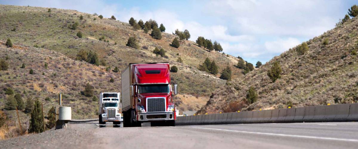 Semi trailers going on straight highway road with poor plants covered hills in Idaho