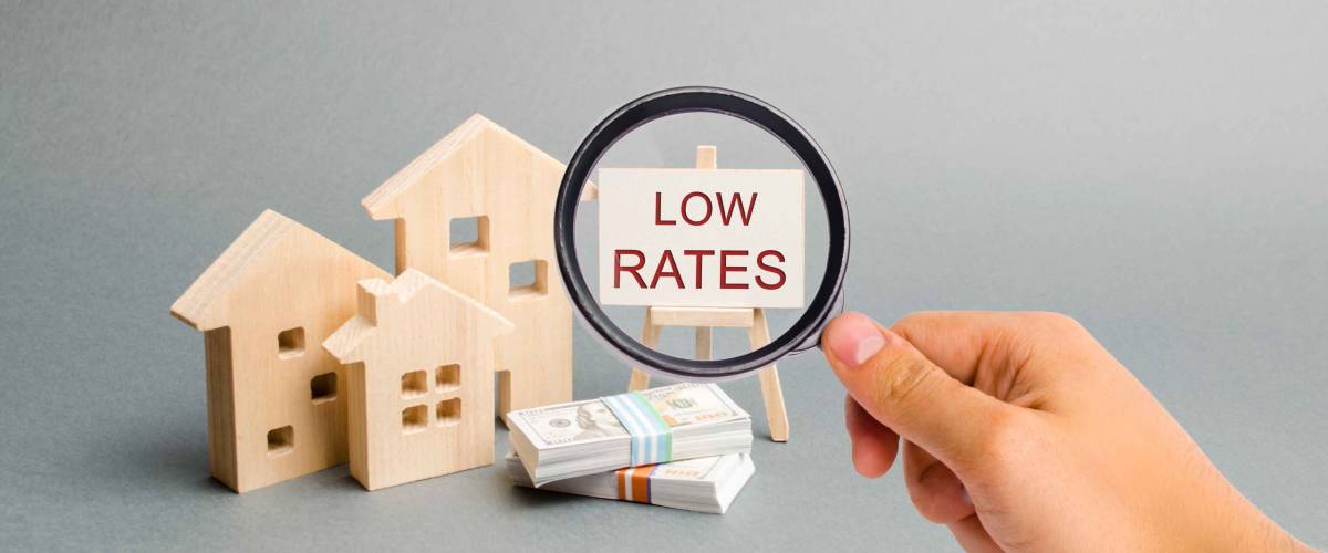A magnifying glass is looking at a poster with the word Low rates and wooden house.