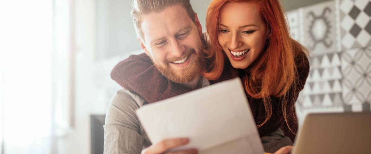 Photo of a positive young couple embracing and calculating the bills at home.