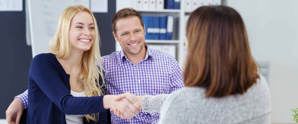 Happy couple shaking hands with woman sitting across the table in an office
