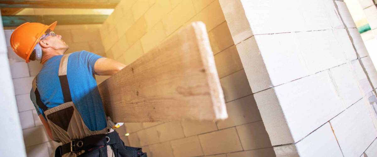 Construction Worker with Large Plank Inside House Build