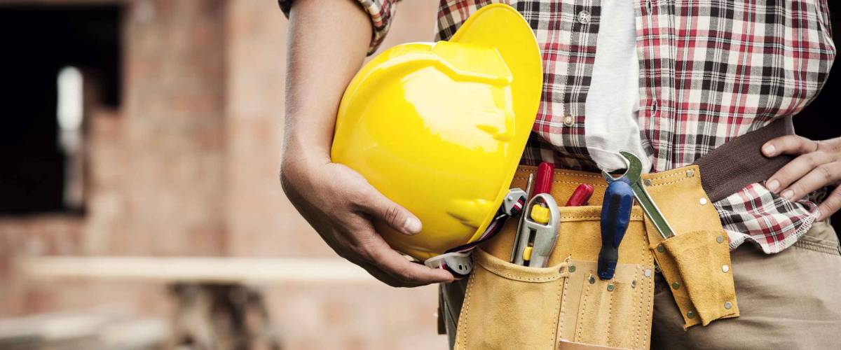 Construction Worker holding hardhat at hip, with toolbelt on waist