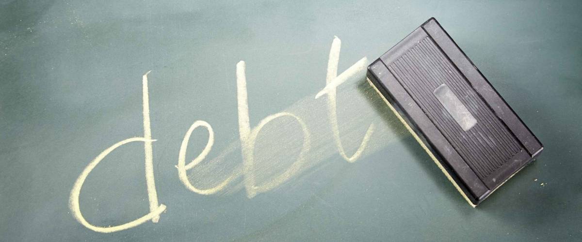 word DEBT written in chalk on a blackboard being rubbed out by an eraser