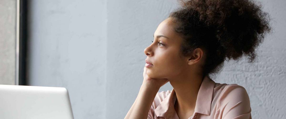 Close up portrait of a young african american woman looking out window when working on laptop