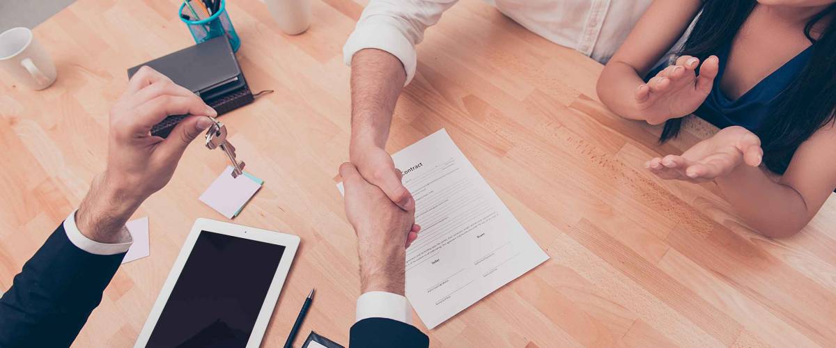 Broker giving keys of new house and shaking hands with customer, seen from above