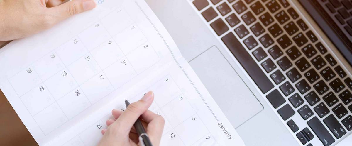 woman writing into agenda with laptop in front of it