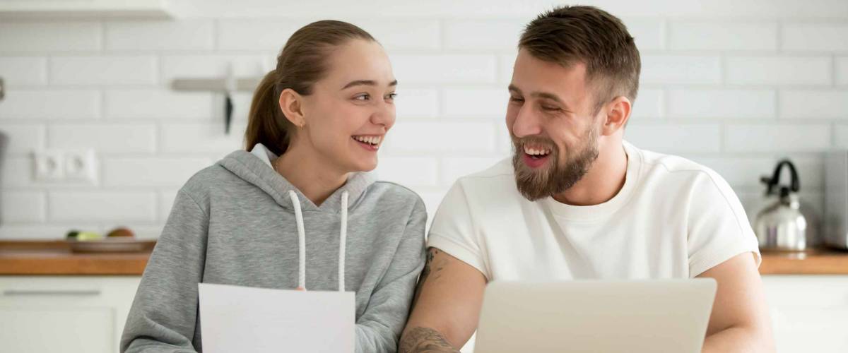 Young smiling happy couple talking at home in the kitchen with laptop papers,