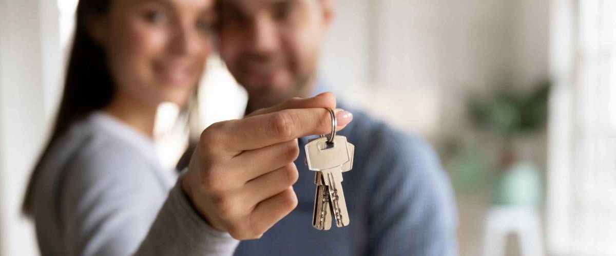 Close up happy woman hugging man, holding keys from new first house, young family celebrating moving day, satisfied customers couple purchase real estate, mortgage and relocation concept
