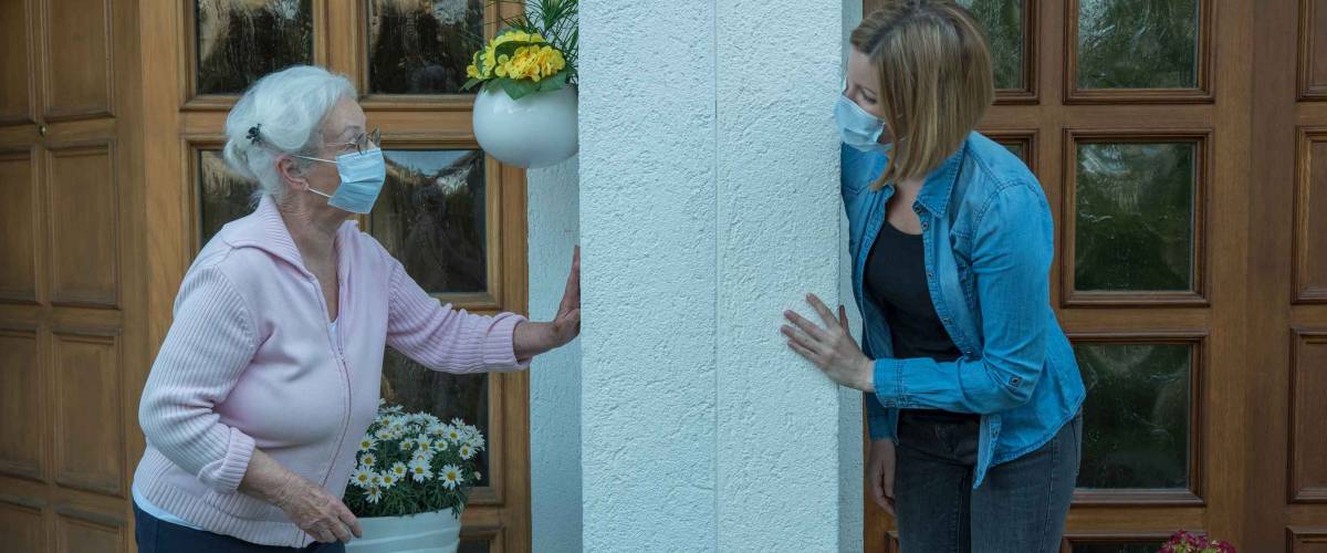 Senior woman with face mask in house quarantine talks to neighbor at safety distance
