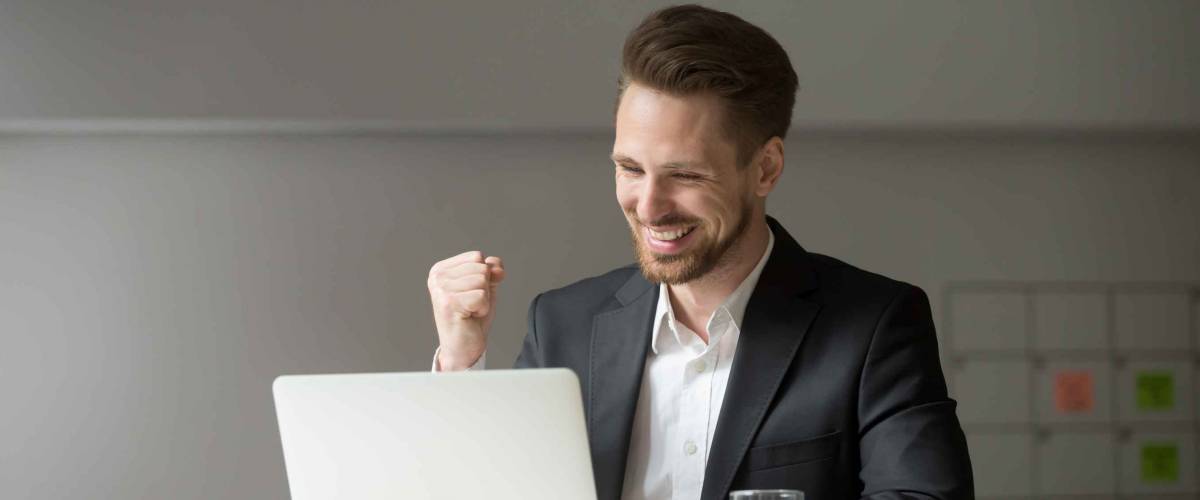 Happy young businessman in suit looking at laptop excited