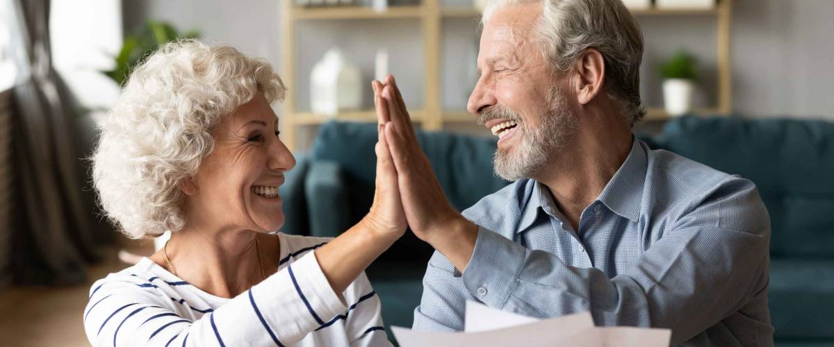Excited older couple giving high five, mature family celebrating success, checking or paying domestic bills, planning budget, smiling mature man holding financial documents, reading good news