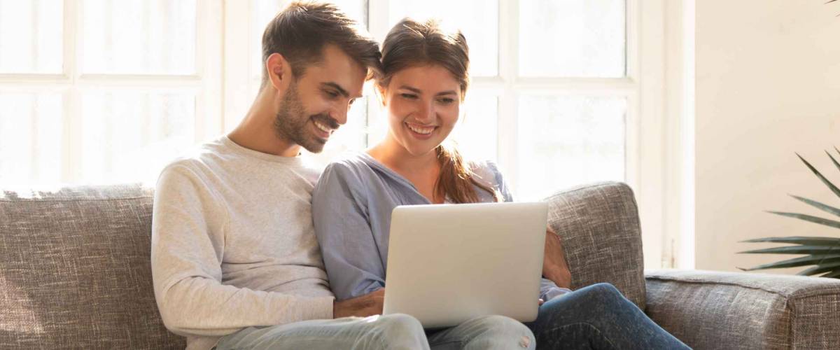 Millennial happy couple using laptop, checking online house listings.