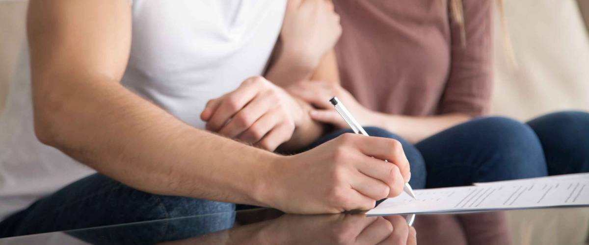 Close up of couple signing documents, making an offer on their first home.