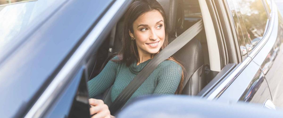 Young woman driving a car in the city. Portrait of a beautiful woman in a car, looking out of the window and smiling. Travel and vacations concepts