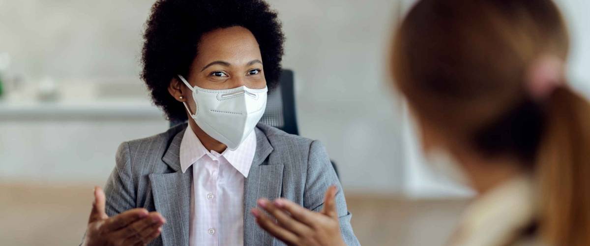African American bank manager with protective face mask communicating with her client during a meeting in the office.