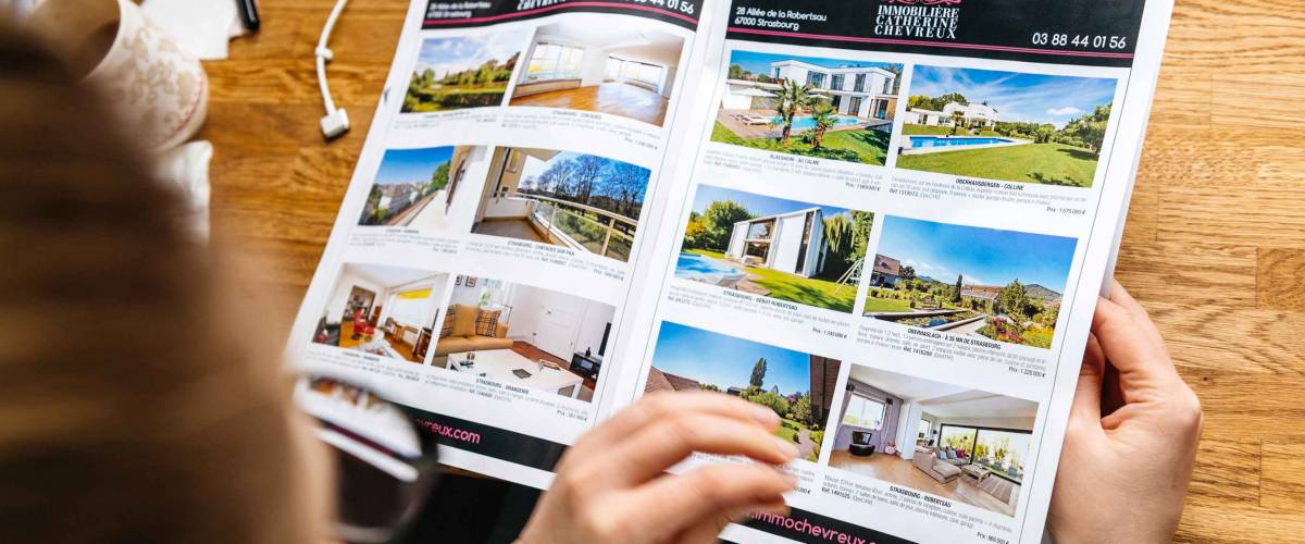 PARIS, FRANCE - APR 26, 2017: View from above of woman reading Houses and Apartments real estate catalogue with properties for rent and buy in France, Alsace Maisons Alsace