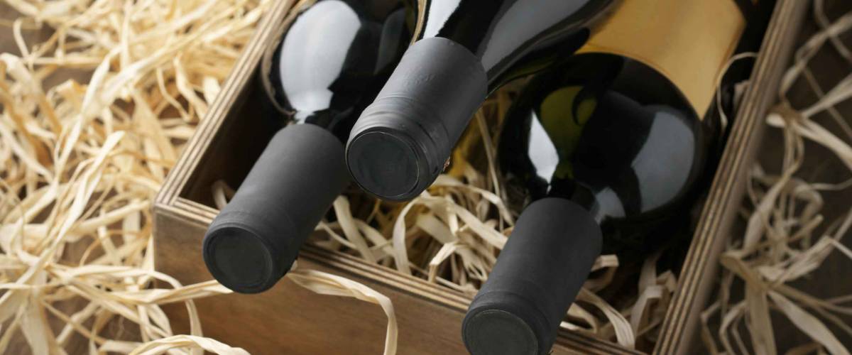 Three closed wine bottles lying on straw in vintage wooden box.