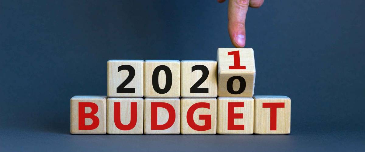 Business concept of planning 2021. Male hand flips wooden cube and change the inscription 'BUDGET 2020' to 'BUDGET 2021'. Beautiful grey background, copy space.