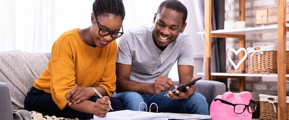 Young African Couple Sitting On Sofa Calculating Invoice