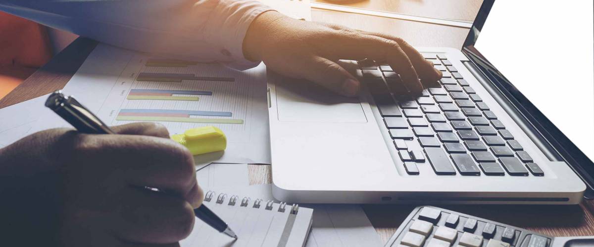 Man using one hand to look at laptop, other to write notes