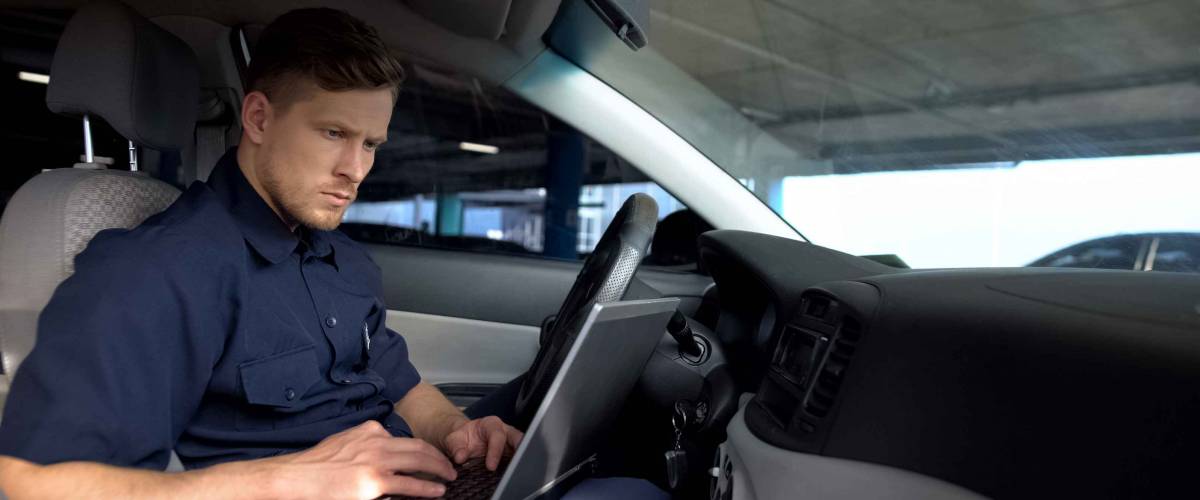 Male police officer working on laptop in car, filling data in crime report