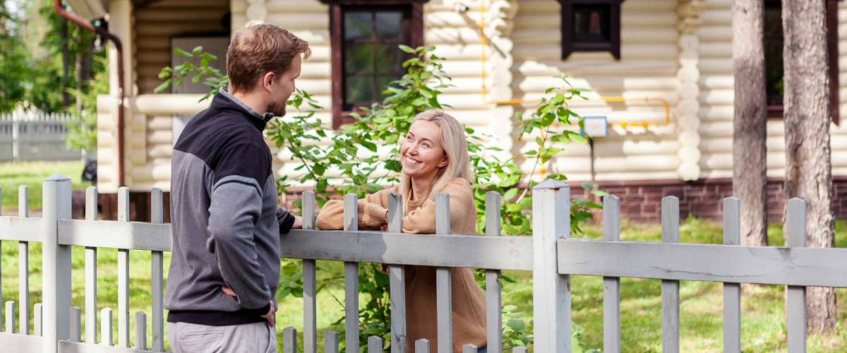 Man and woman chat amiably over grey wood fence