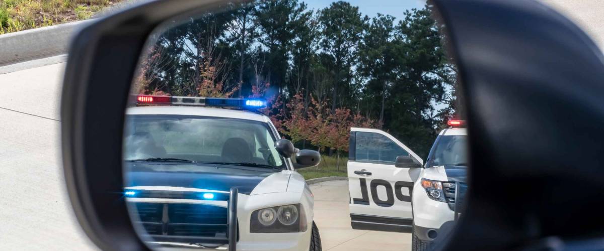 Two police cruisers seen through car's side mirrors