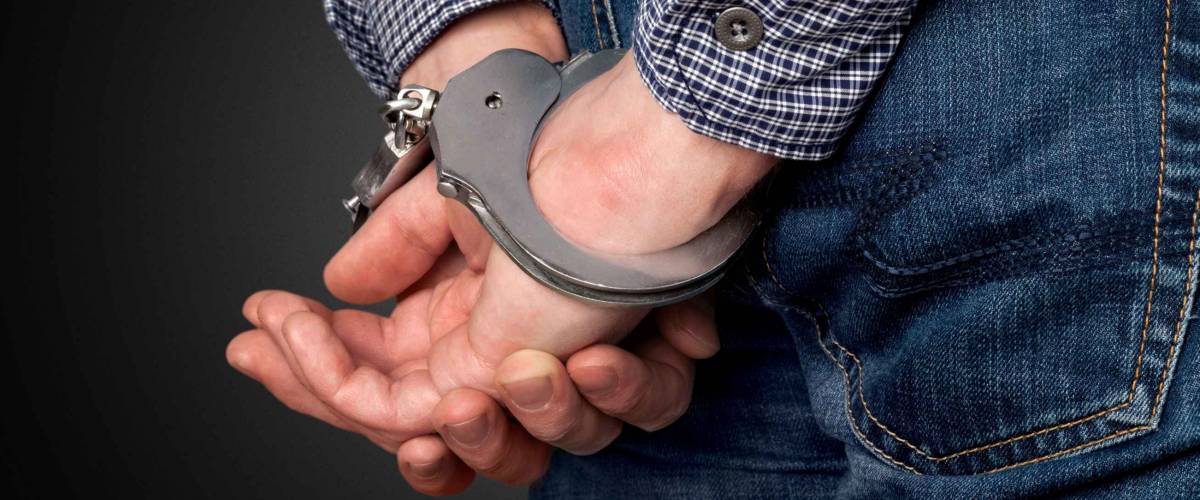 Close up of man's hands behind his back with handcuffs on