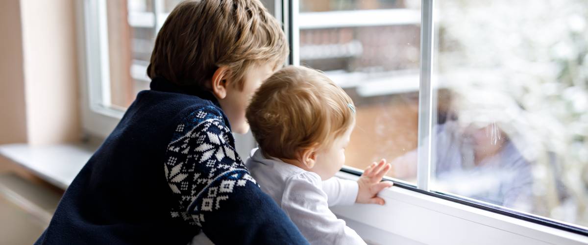 Two kids look out window of home in winter