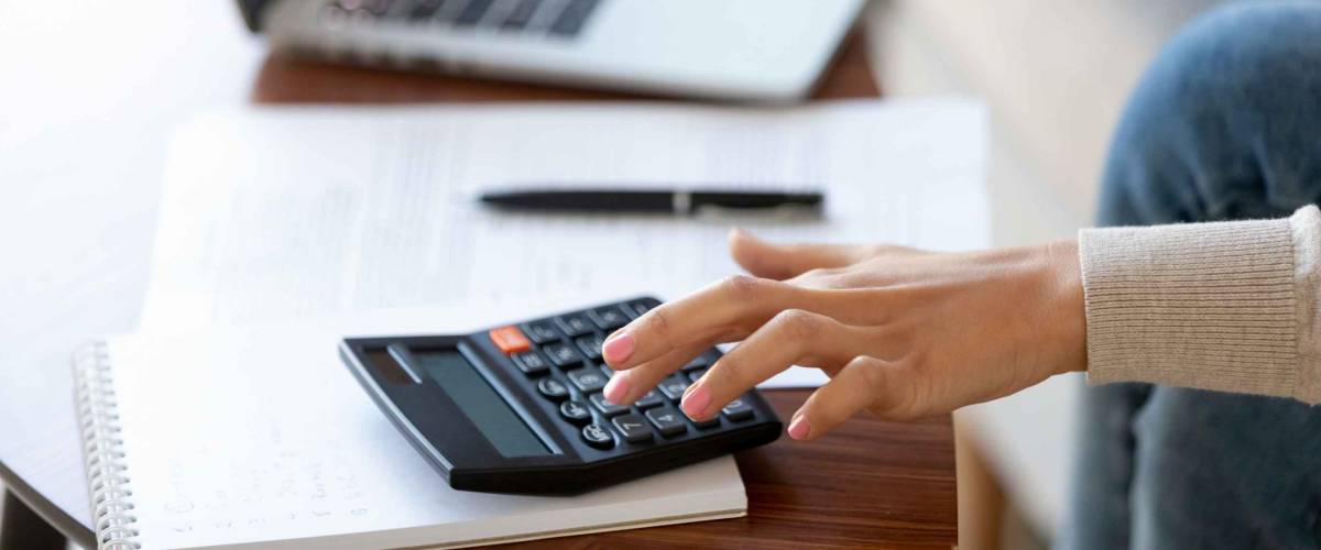 Up close of woman's hand using a calculator on a desk with pen and paper beside it