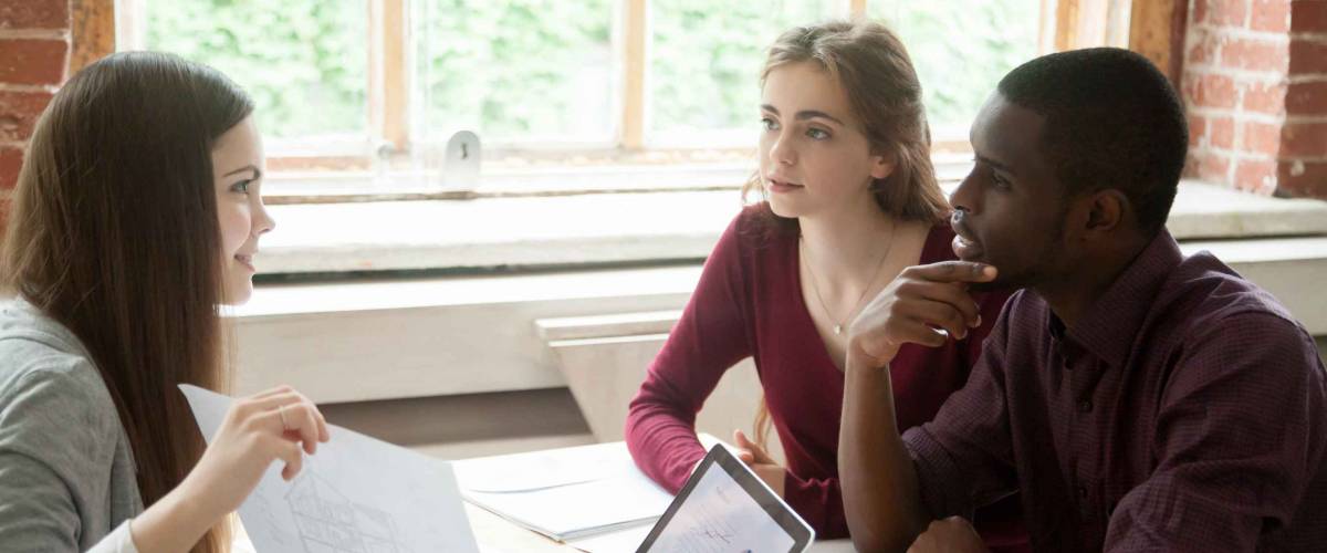 Woman holds up paper to man and woman sitting across from her, explaining something
