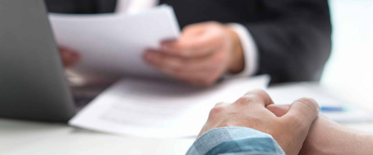 Close up of man in business suit holding paper, across the table is another man with hands crossed