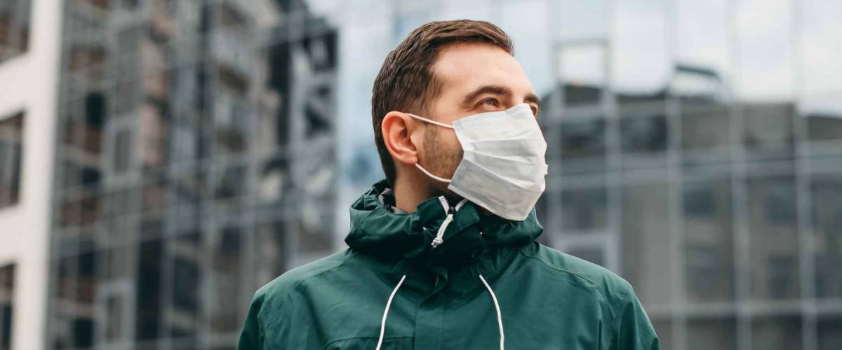 portrait of brunette man in a surgical bandage on a background of a modern building, coronavirus, illness, infection, quarantine, medical mask