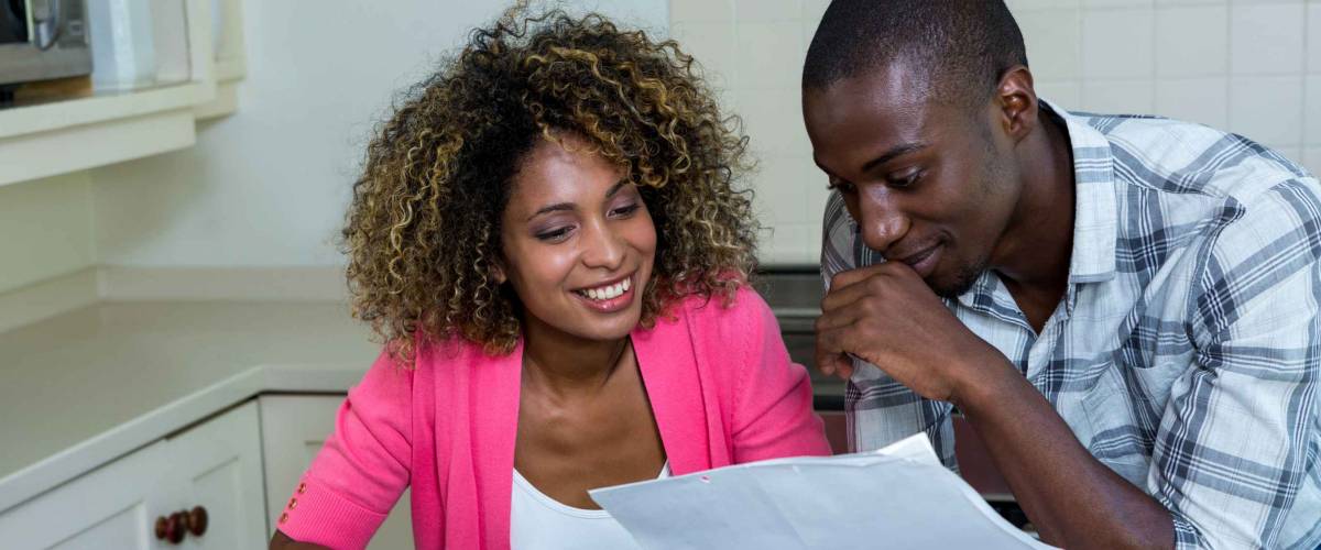 Happy couple checking bills while using digital tablet in kitchen