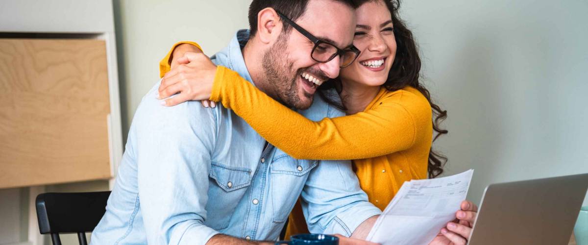 Positive young couple embracing and calculating and paying bills on laptop online at home stock photo