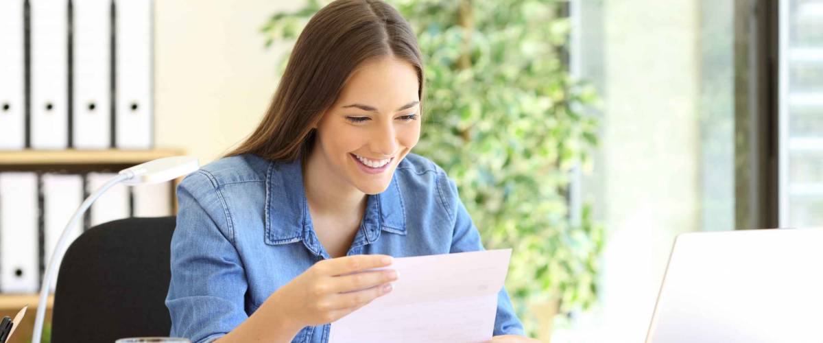 Happy entrepreneur woman reading good news in a letter in a desk at office
