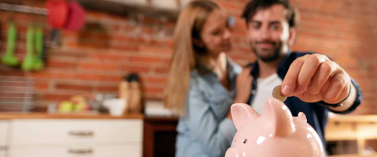 Happy couple inserting coin in piggybank. Home budget, family finance concept. Wide photo with space for your text
