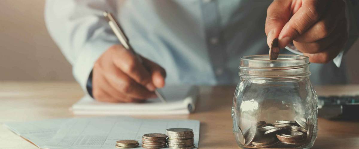 Close up of man's hands writing notes and dropping coins into a jar