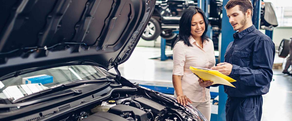 Woman listens to mechanic talking in front of open car