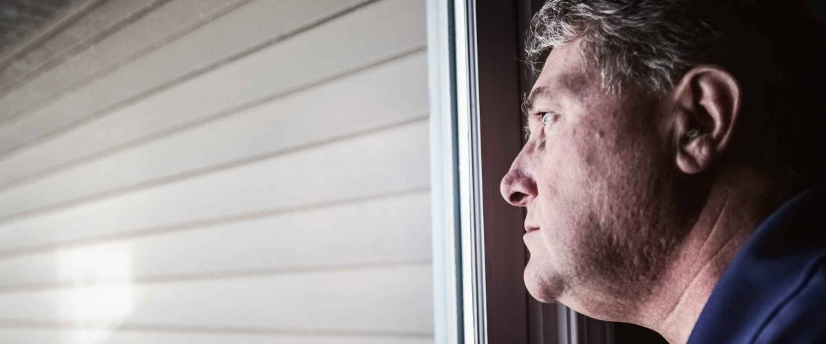 Middle aged man looking out the window, depression and loneliness. Shallow focus on man's nose, reflection in window