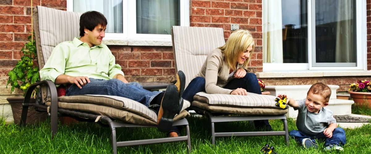 Happy family relaxing in backyard of new home with toddler
