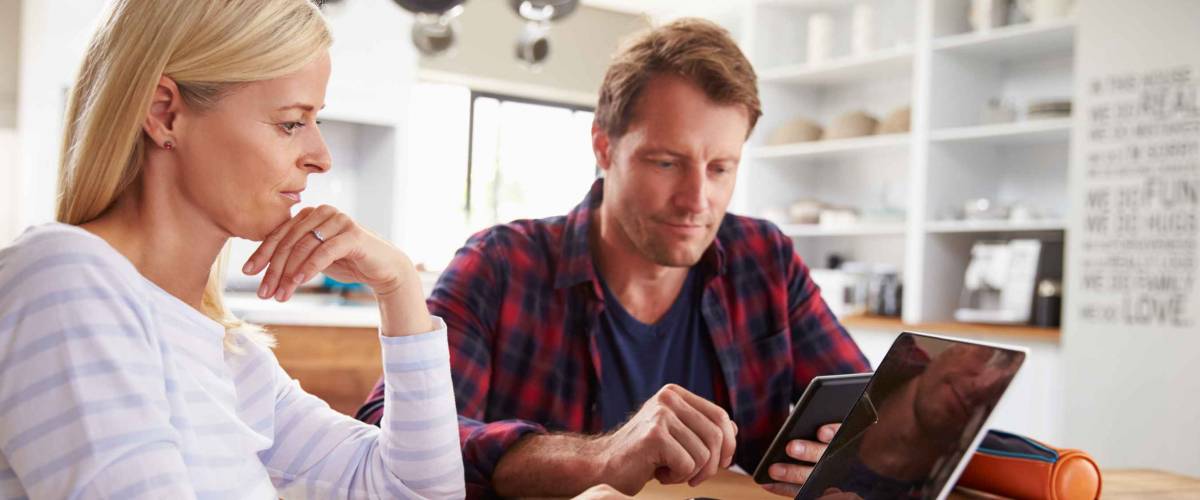 Stressed couple sitting in their kitchen using computers