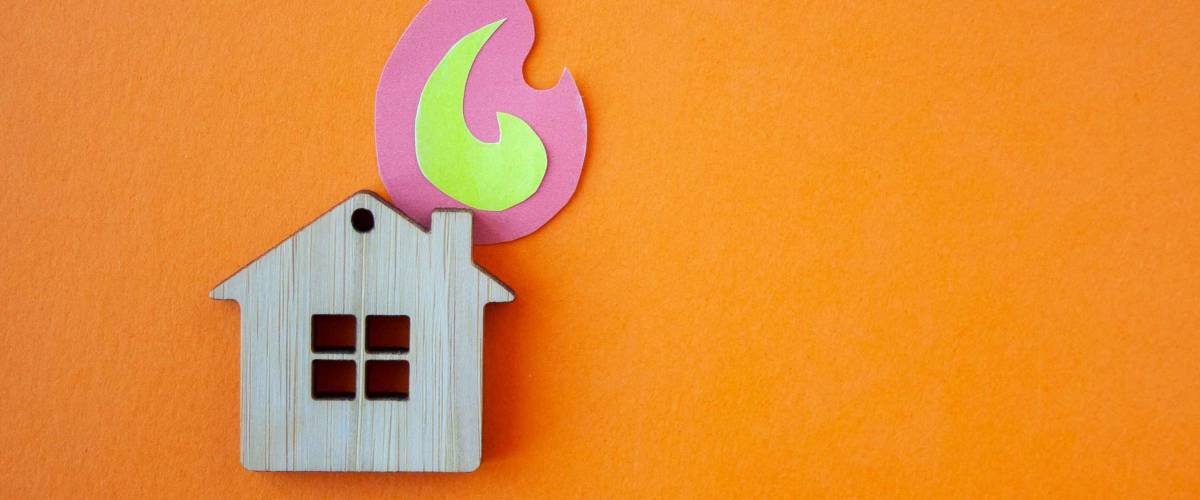 Fire house, insurance and mortgage concept. Small wooden house toy and paper fire shape on orange background top view with copy space