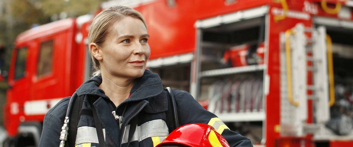 Portrait of young woman firefighter standing near fire truck.
