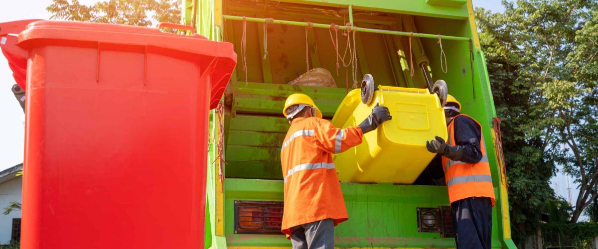 Two garbage men working together on emptying dustbins for trash removal with truck loading waste and trash bin.